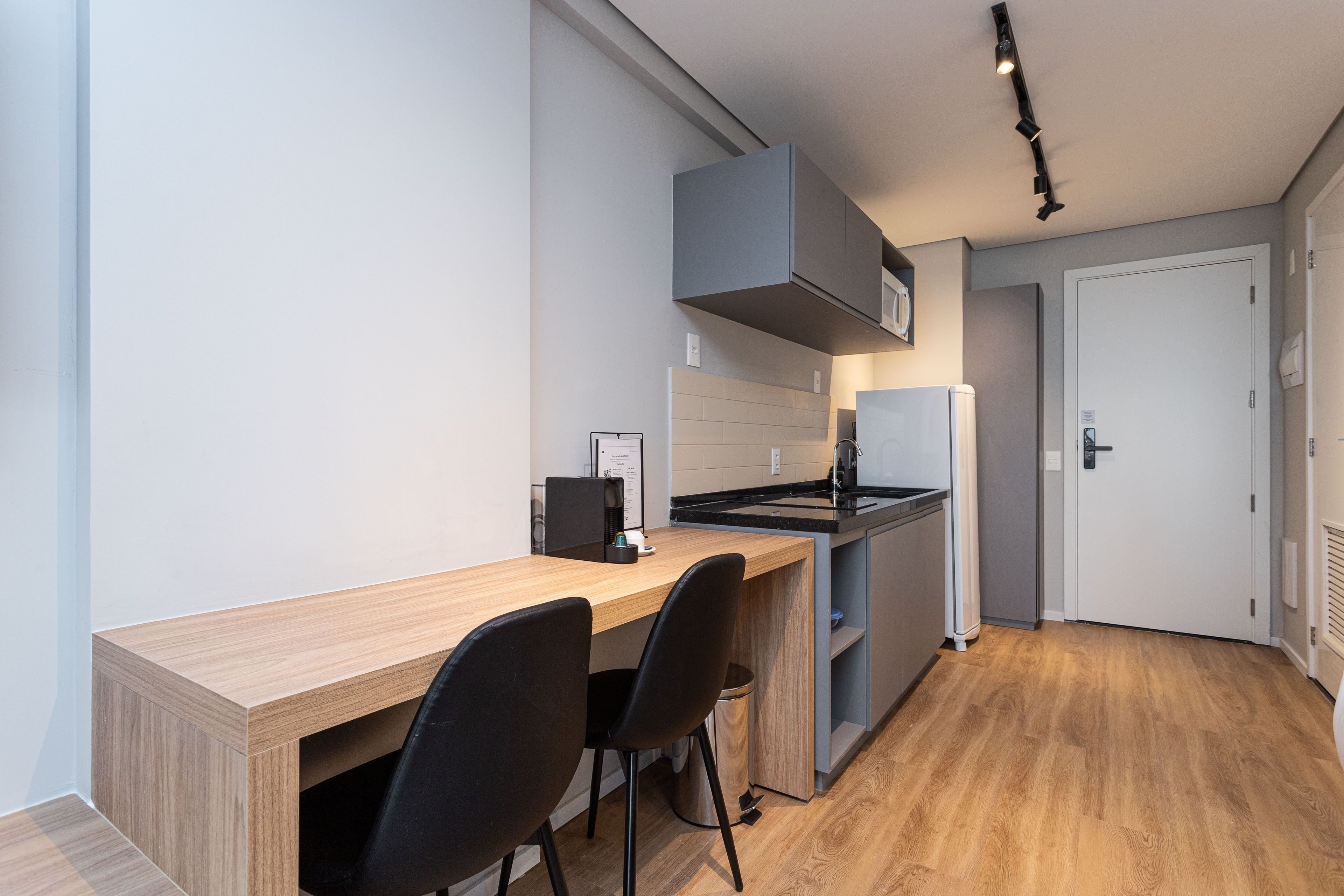 A modern kitchen with a wooden countertop, two black chairs, a built-in oven, and a grey cabinet above the sink.