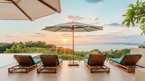 A terrace with lounge chairs and a large umbrella, overlooking a scenic view.