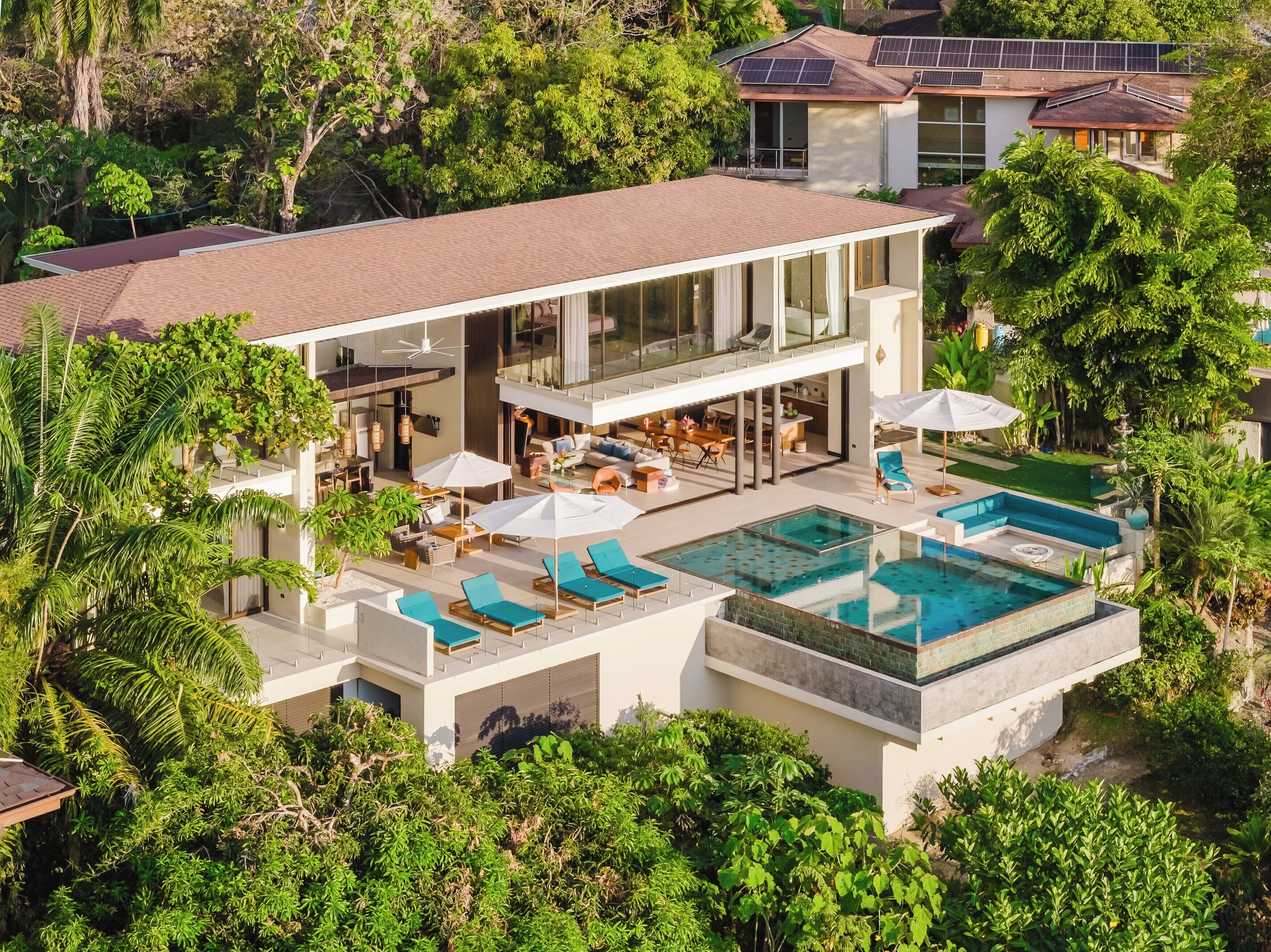 A modern house with a large outdoor pool, multiple seating areas, and a covered patio.