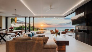 A modern living room with a large sofa, a dining area, and a TV mounted on a wall.