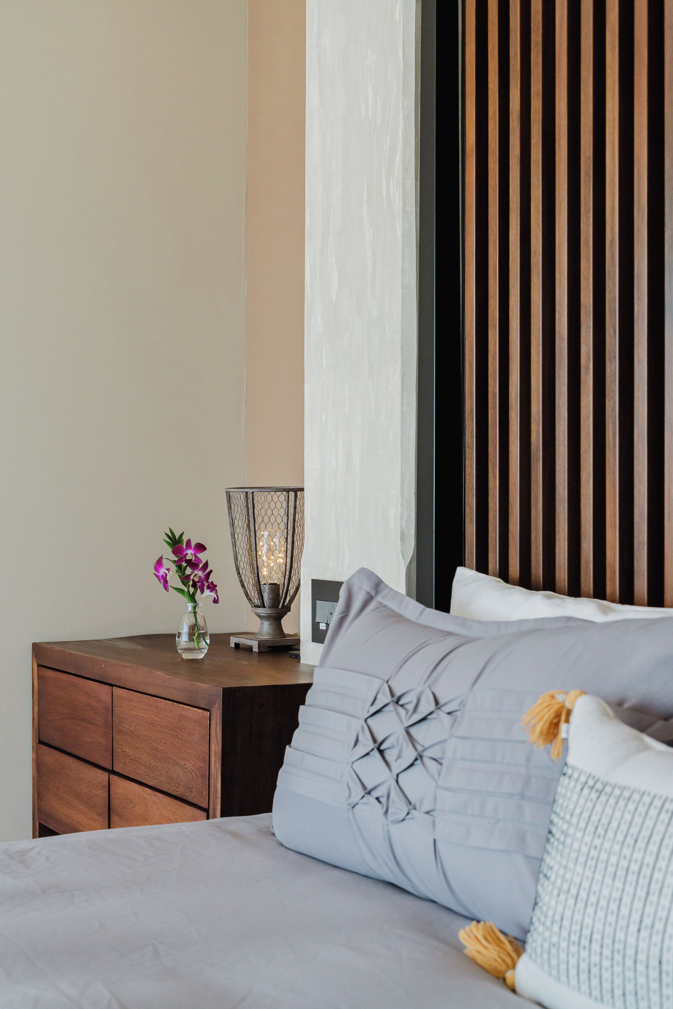 Een netjes ingerichte hotelkamer met een bed, een nachtkastje, een vaas met bloemen en een wandlamp.