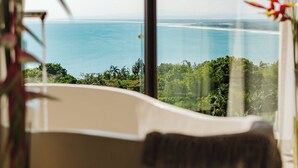 A bathtub with a view of the ocean and greenery.