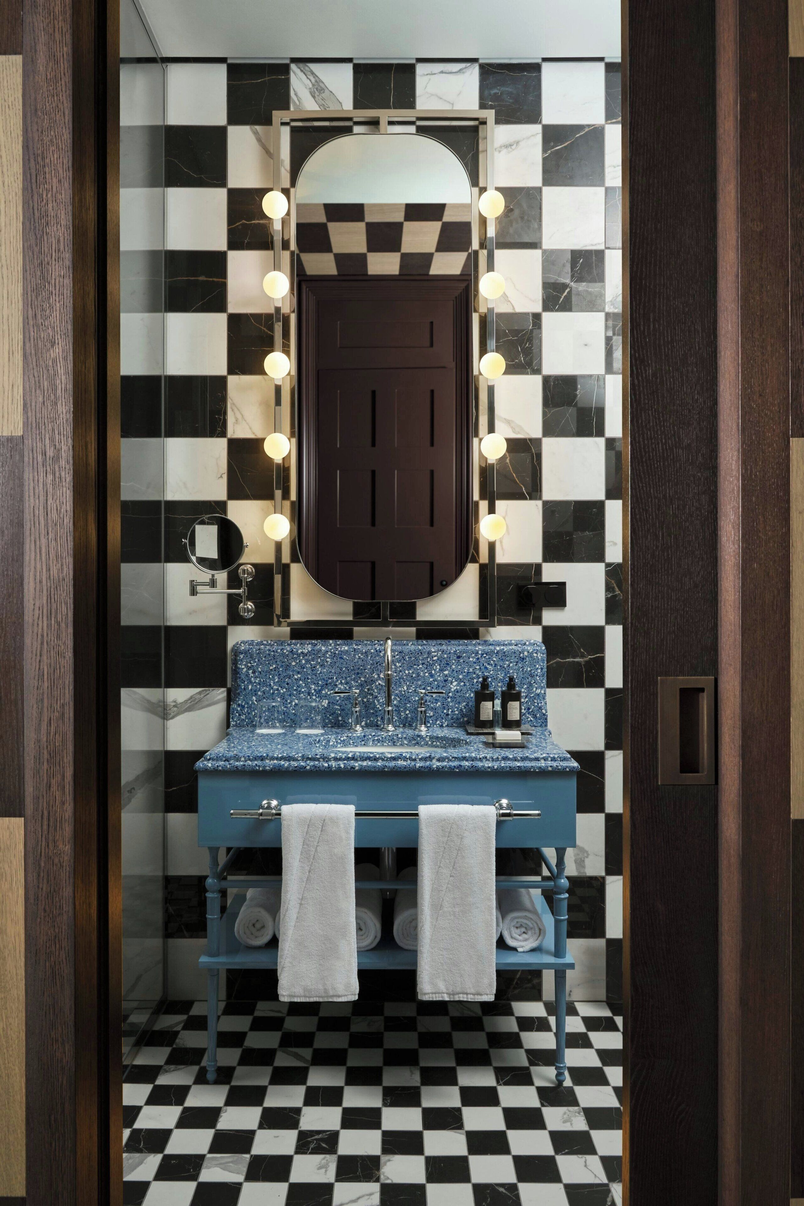 Een badkamer met een zwart-wit geruite vloer, een blauwe wastafel met een marmeren aanrechtblad en een spiegel met verlichting erboven.