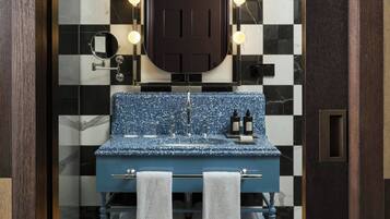 Un baño con piso a cuadros blanco y negro, un lavamanos azul con encimera de mármol y un espejo con luces arriba.