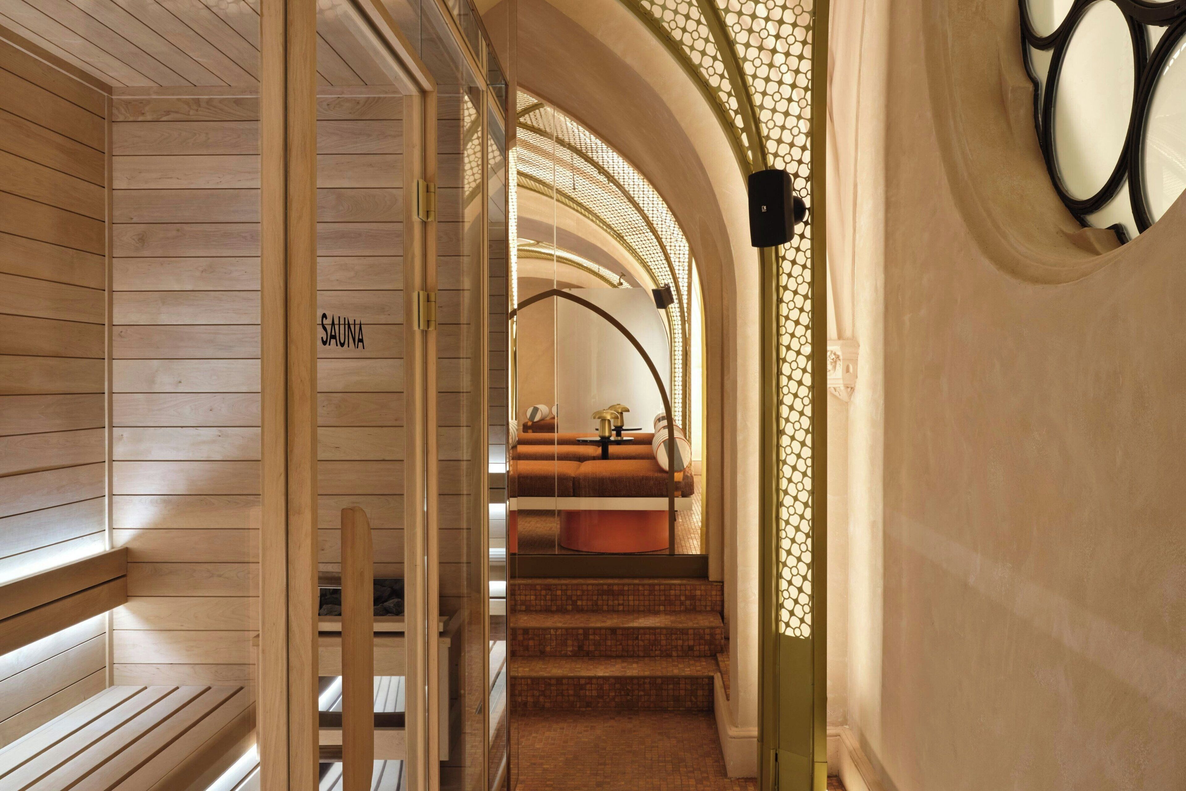 Un couloir intérieur en bois, avec un panneau indiquant la présence d’un sauna, un escalier et un mur orné d’un motif.