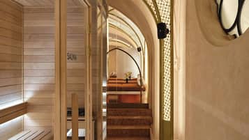 Un couloir intérieur en bois, avec un panneau indiquant la présence d’un sauna, un escalier et un mur orné d’un motif.