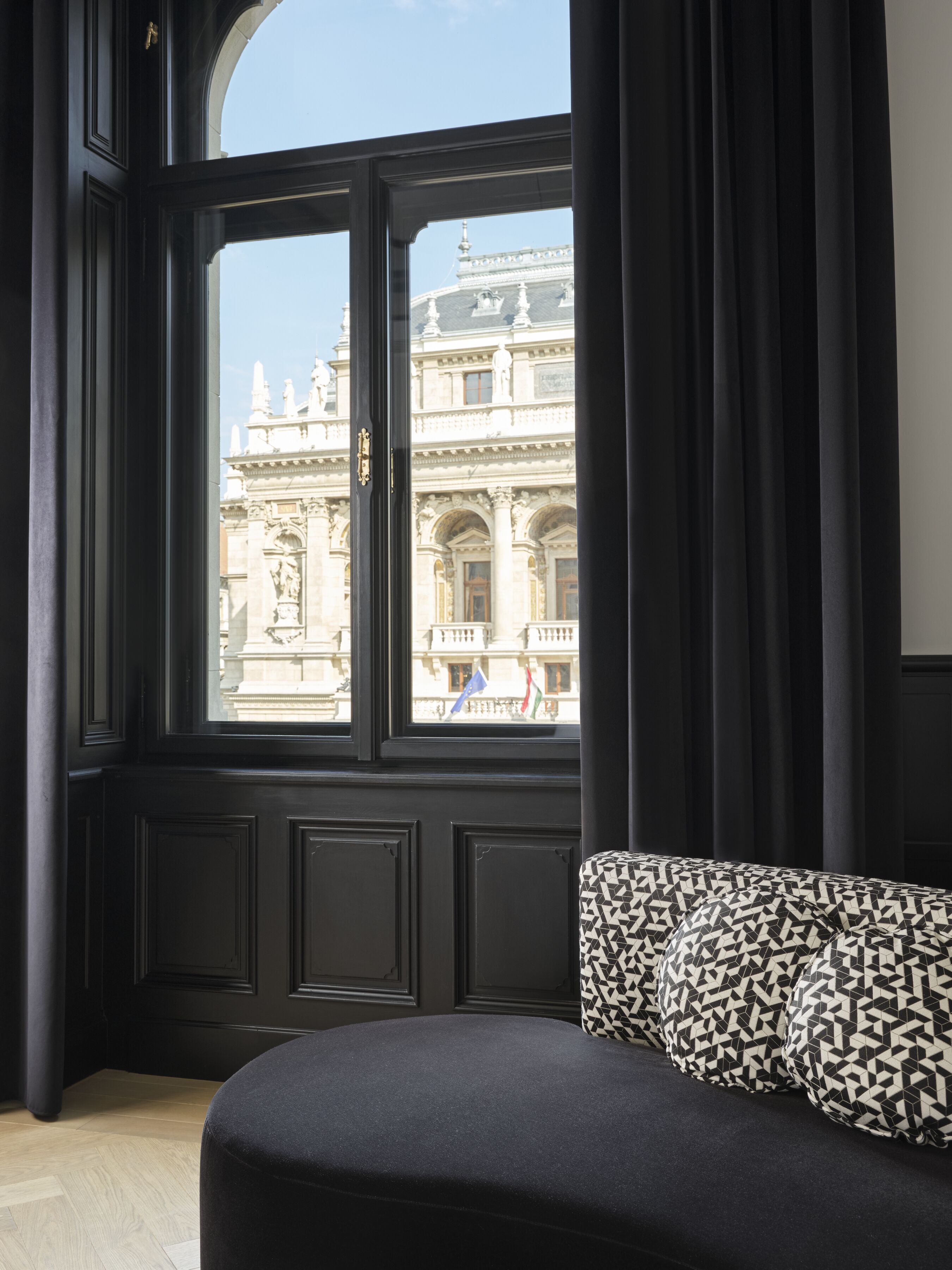 A room with a large window, a black upholstered sofa, and a view of a historic building.