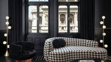A modern room with a black and white houndstooth sofa, a black armchair, and a marble coffee table. Large windows offer a view of a historic building.