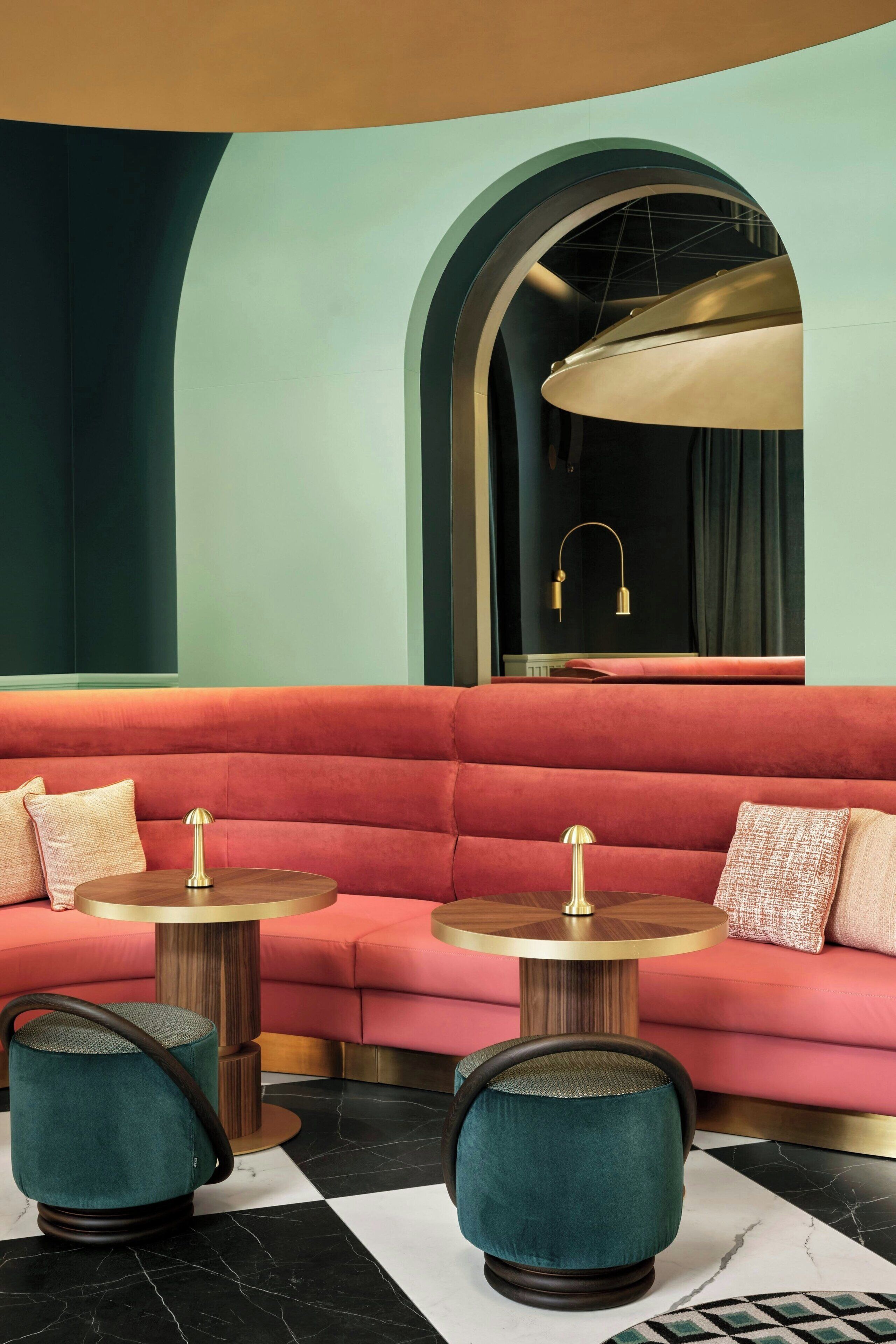 Un espace de détente moderne avec un canapé rouge, deux tables rondes et des poufs turquoise.