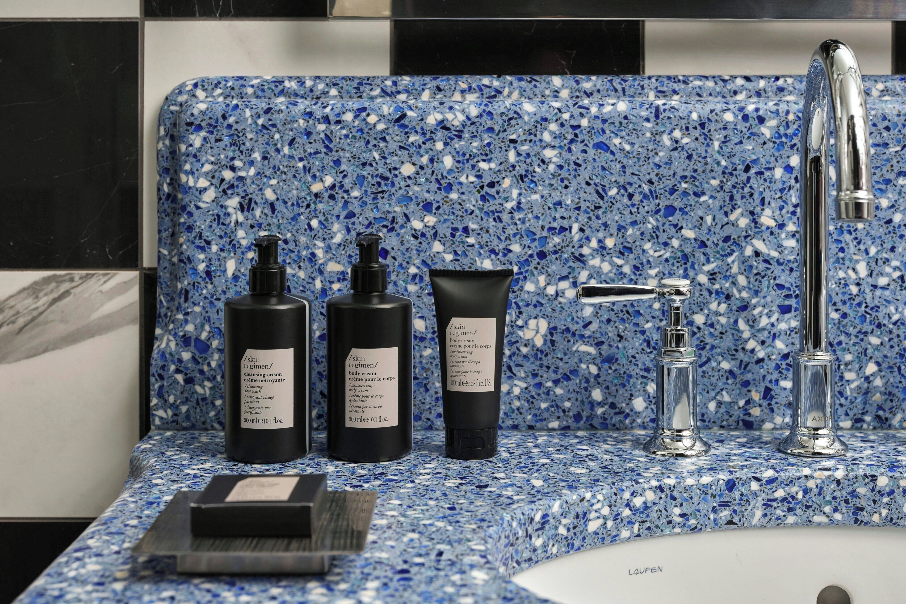 A bathroom with a blue speckled tile backsplash, a chrome faucet, and three black bottles of skincare products on the counter.