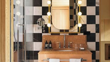 Un baño con piso a cuadros, cabina de ducha de vidrio, tocador con espejo y perchero para toallas.