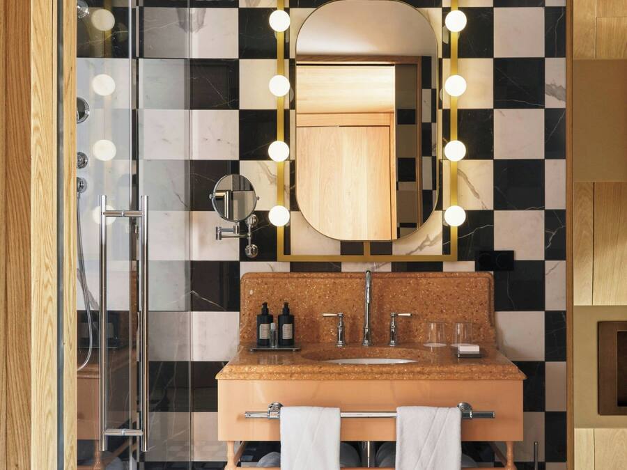 Un baño con piso a cuadros, cabina de ducha de vidrio, tocador con espejo y perchero para toallas.