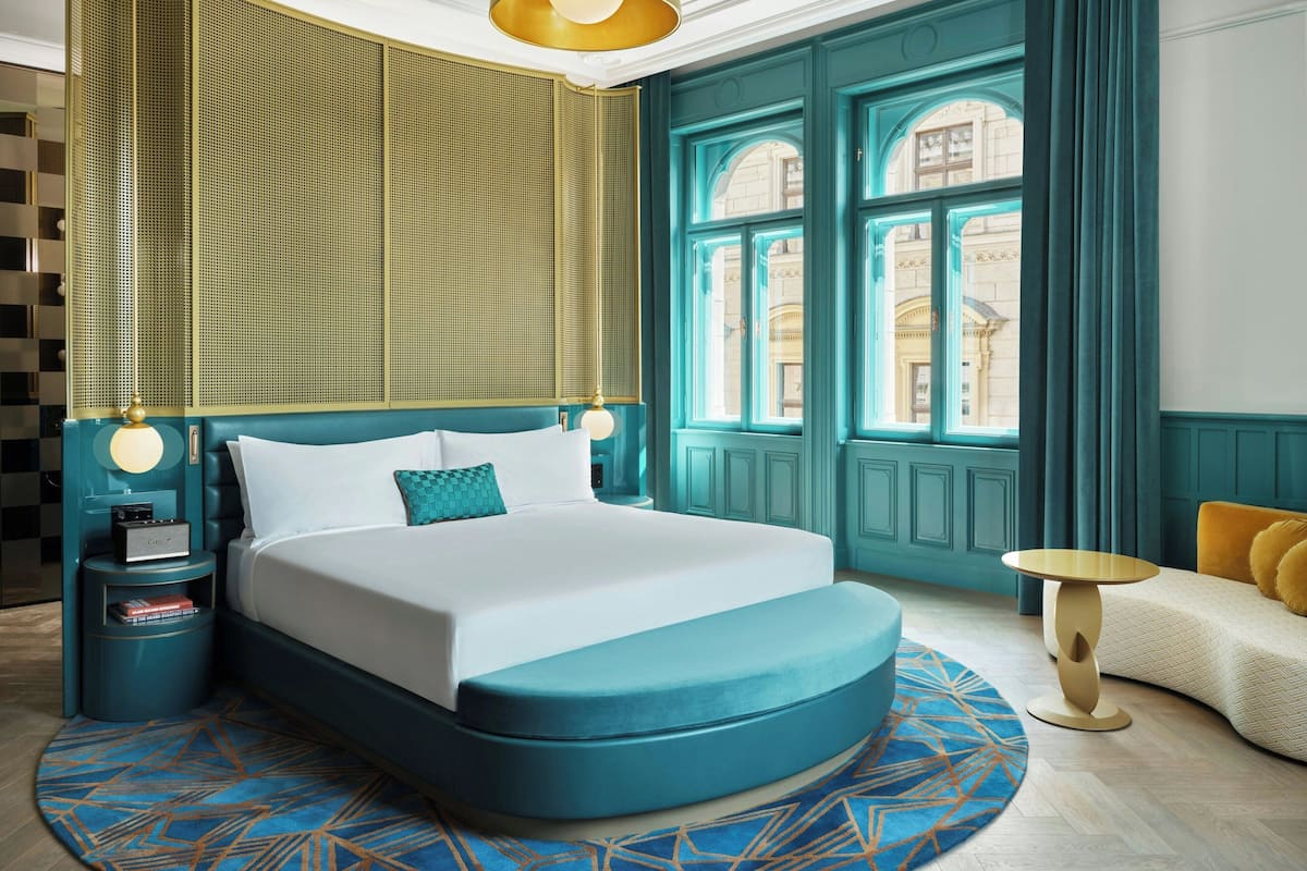 A bedroom with a large bed, a bedside table, a round side table, and a view of the outside through a window.