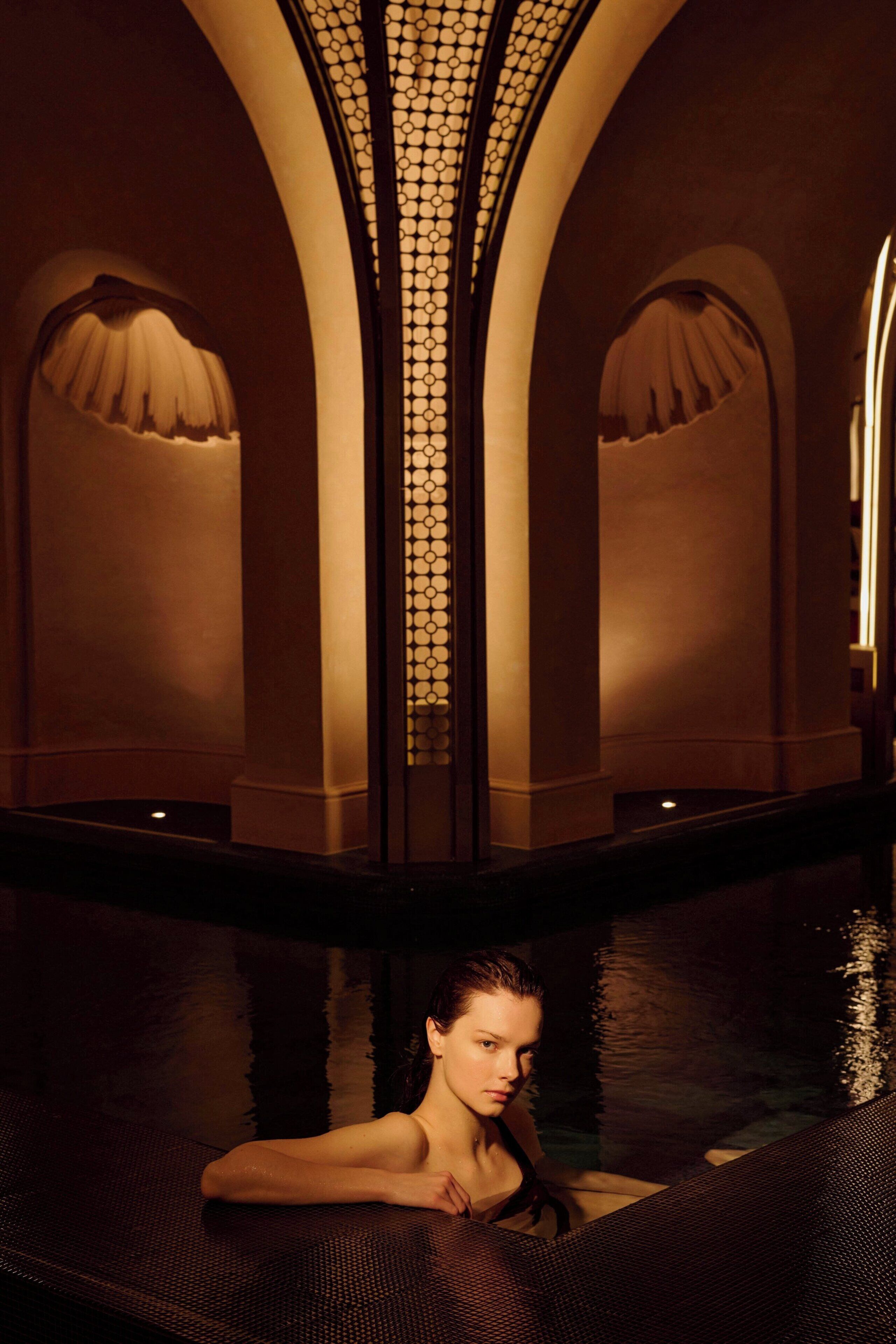 A woman in a pool with arched ceilings and a patterned wall.