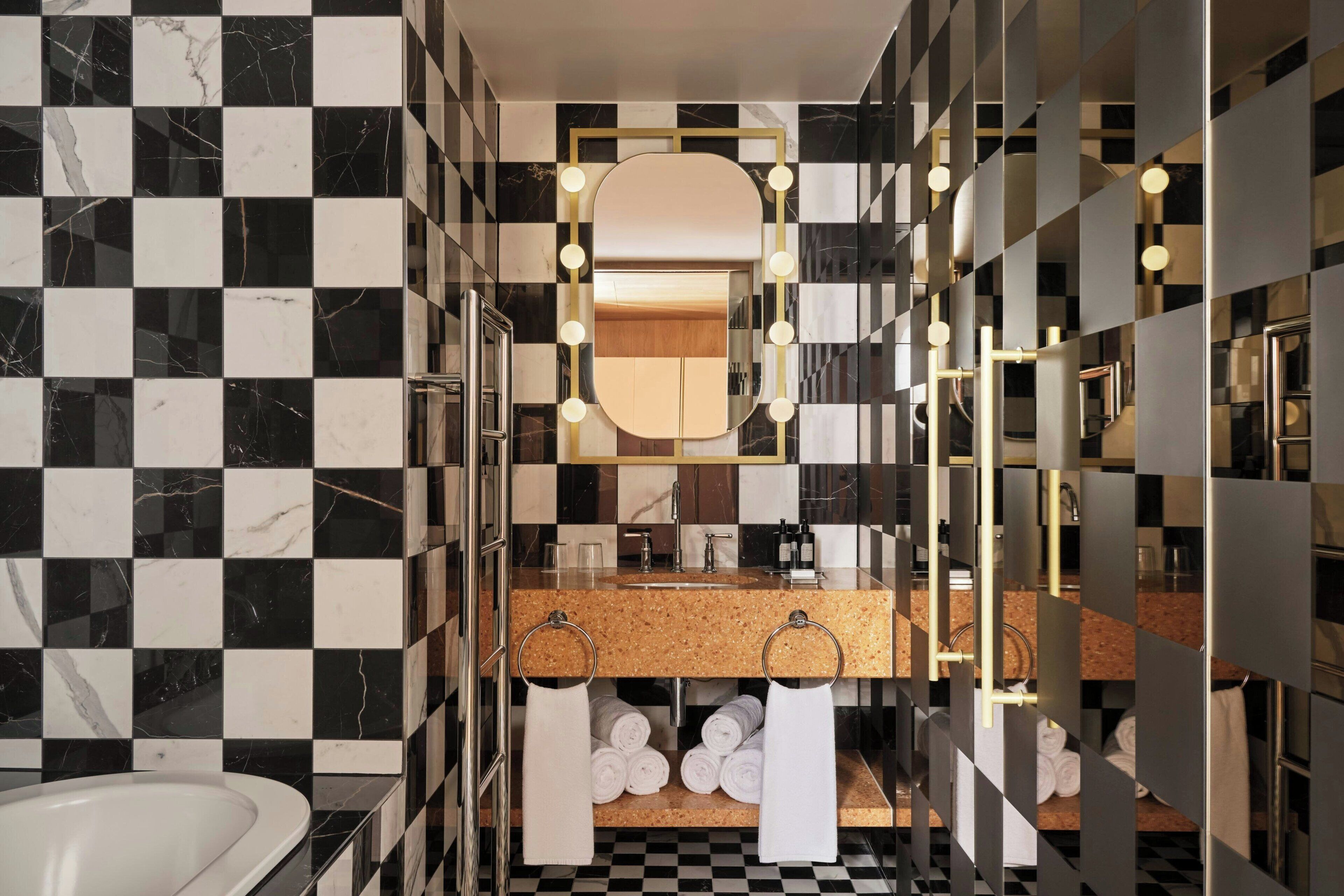 Un bany modern amb un mur d'azulells negres i blancs enquadrats, un mirall amb marc daurat i un lavabo amb taulell de suro.