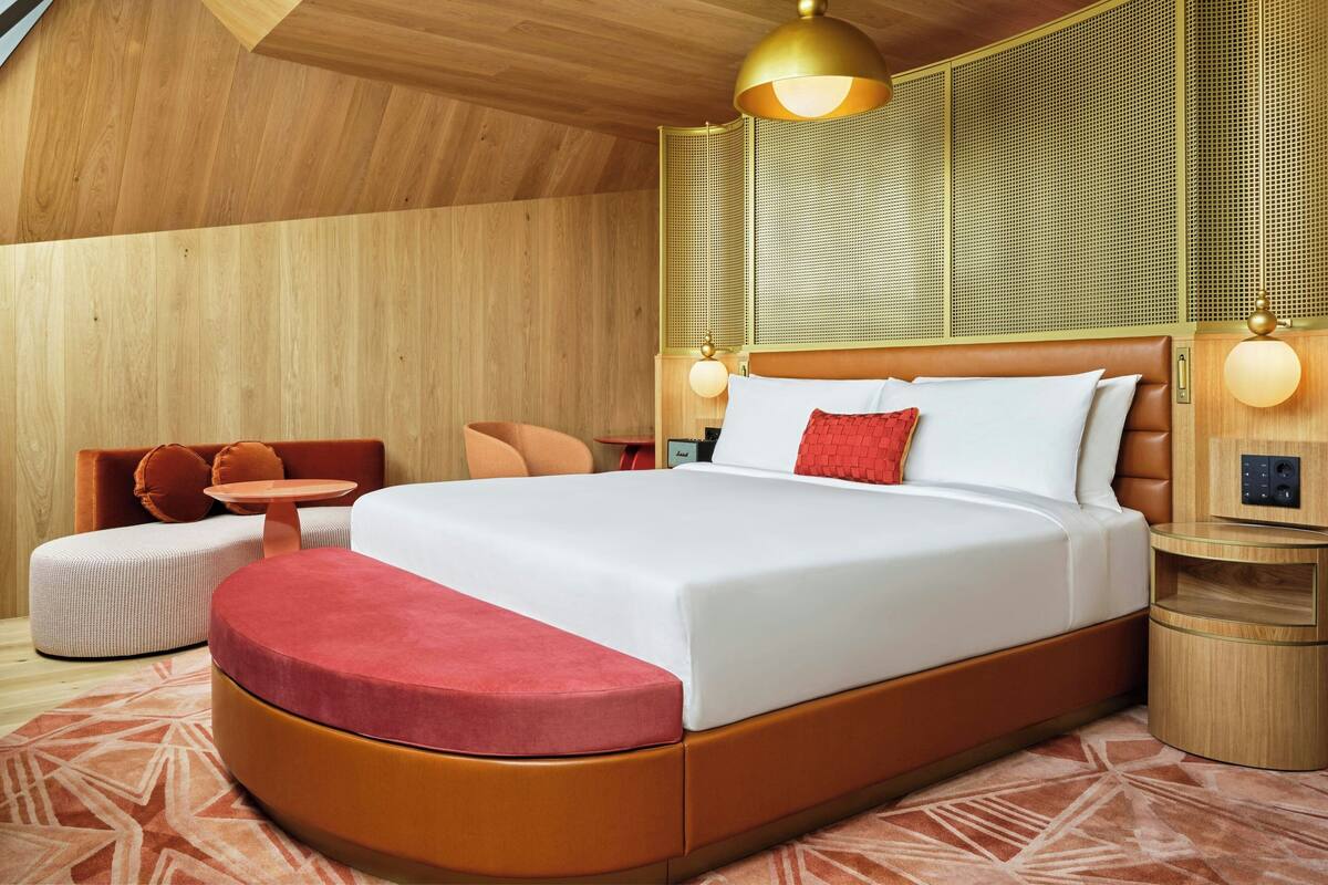 A modern hotel room with a large bed, a seating area with a small table, and a unique ceiling design.