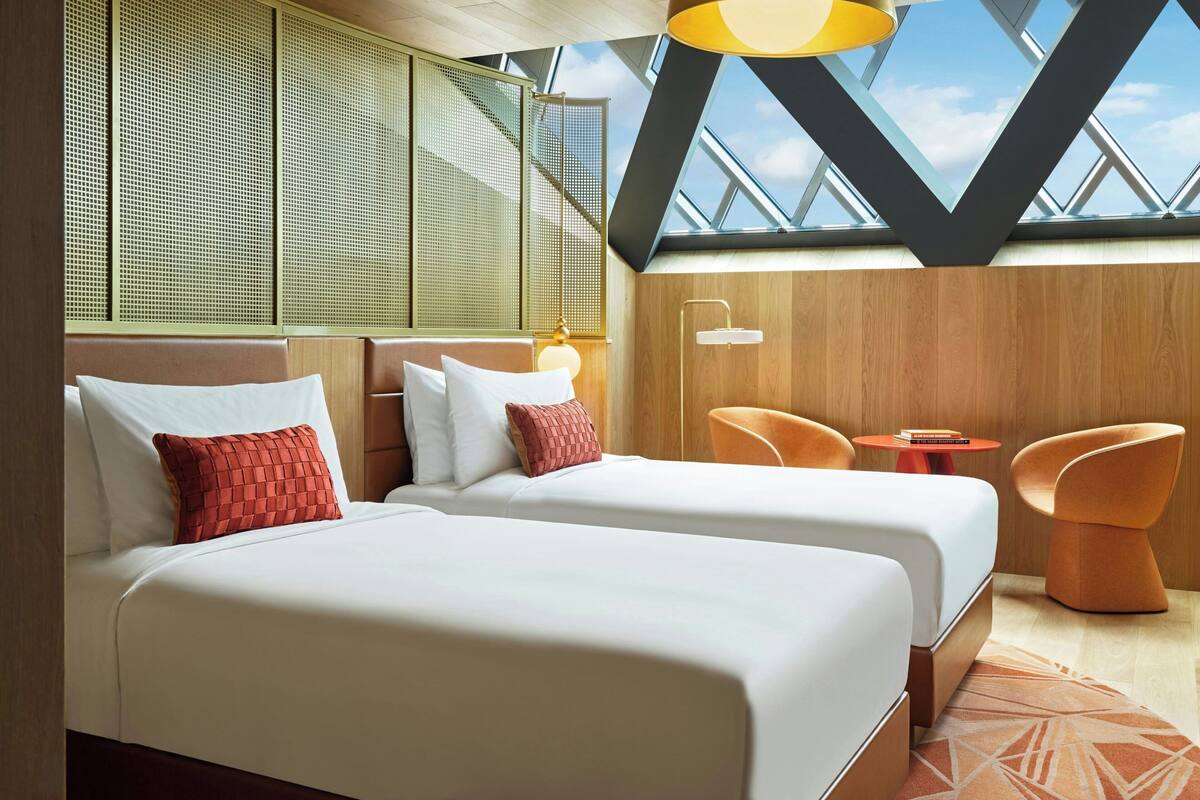 A hotel room with two beds, a small table, and a chair.