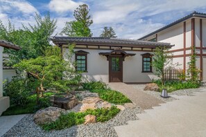 A traditional Japanese-style building with a wooden door, surrounded by a landscaped garden with rocks and greenery.