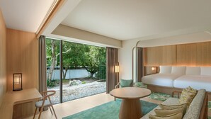 Ein modernes Hotelzimmer mit großem Fenster, einer Couch, einem Bett, einem Schreibtisch und einem Sessel.