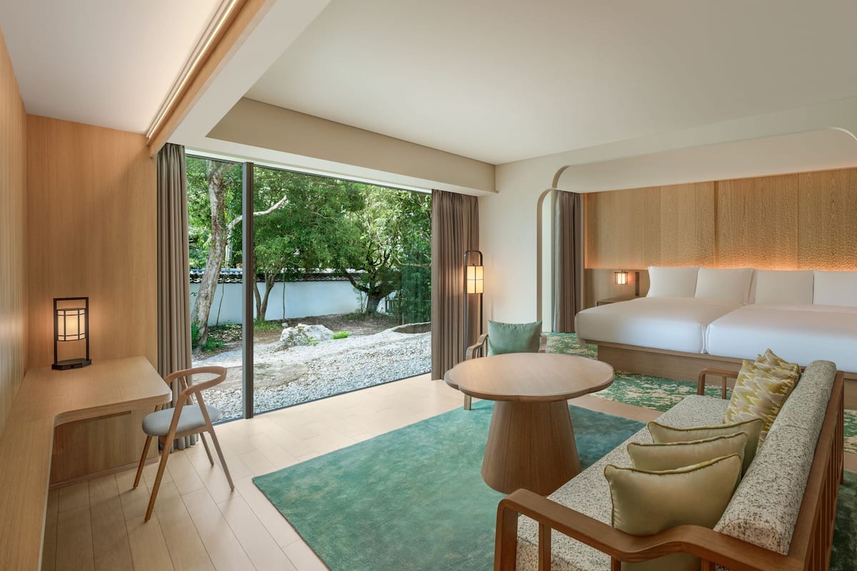 Una habitación de hotel moderna con un ventanal grande, un sofá, una cama, un escritorio y una silla.