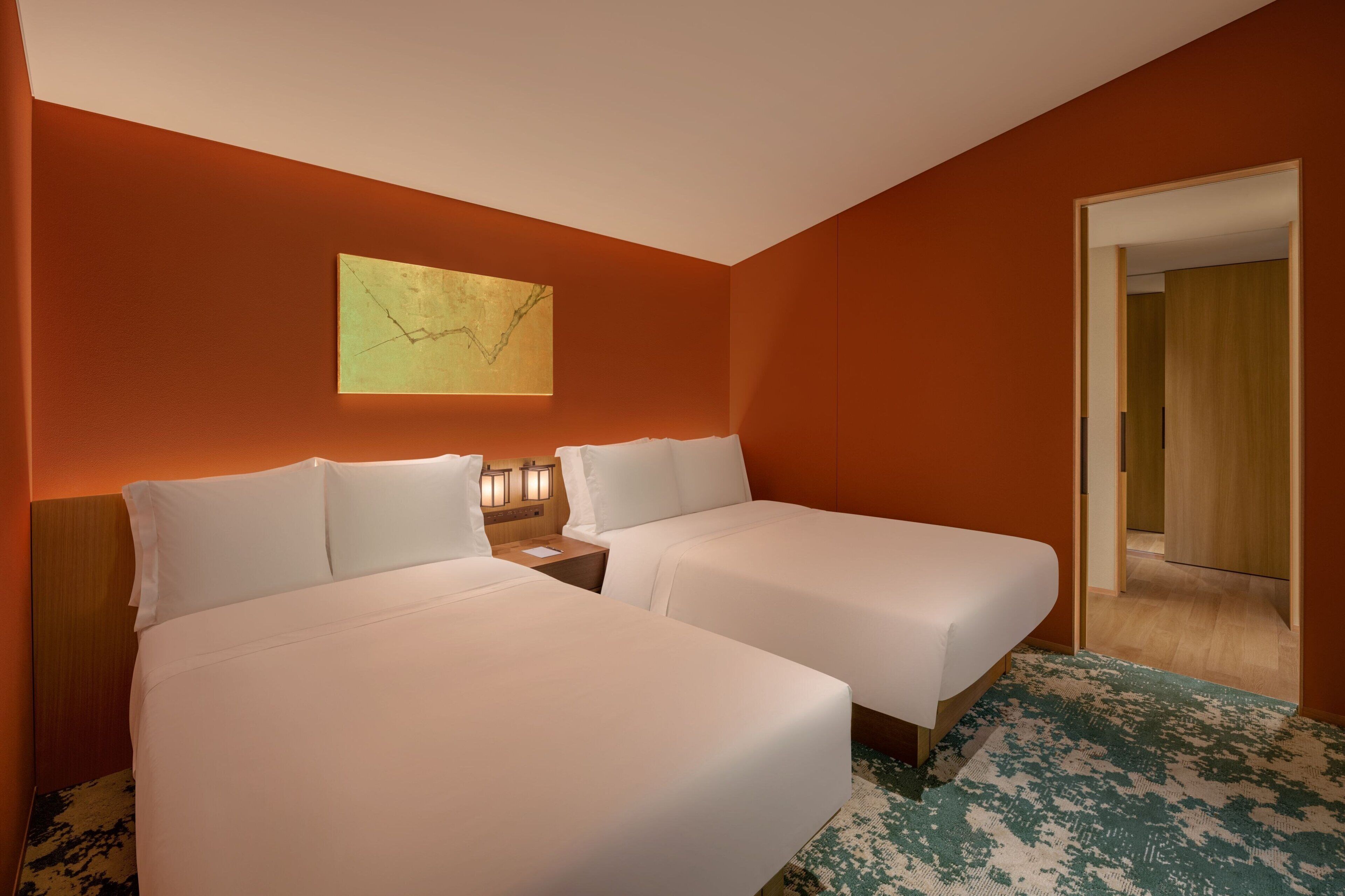 A hotel room with two beds, a painting on the wall, and a wooden door.