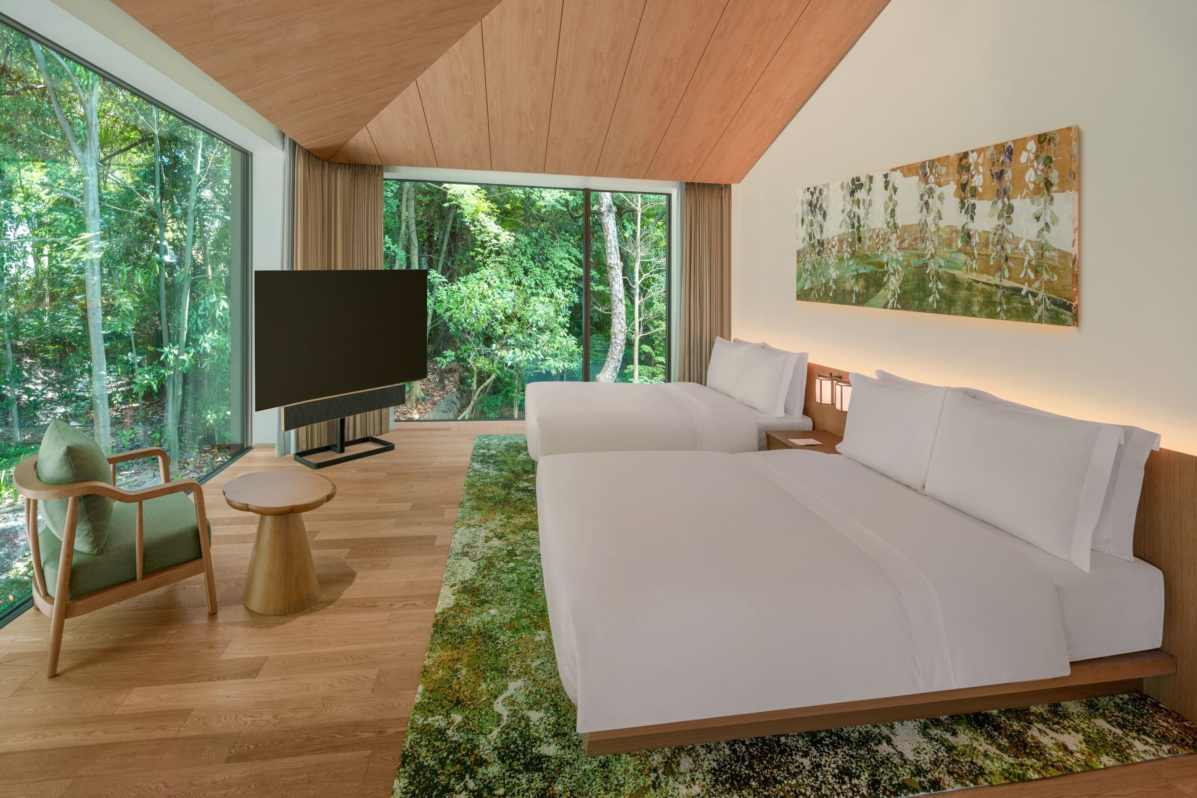 A modern bedroom with a large bed, a TV, and a view of a forest through large windows.