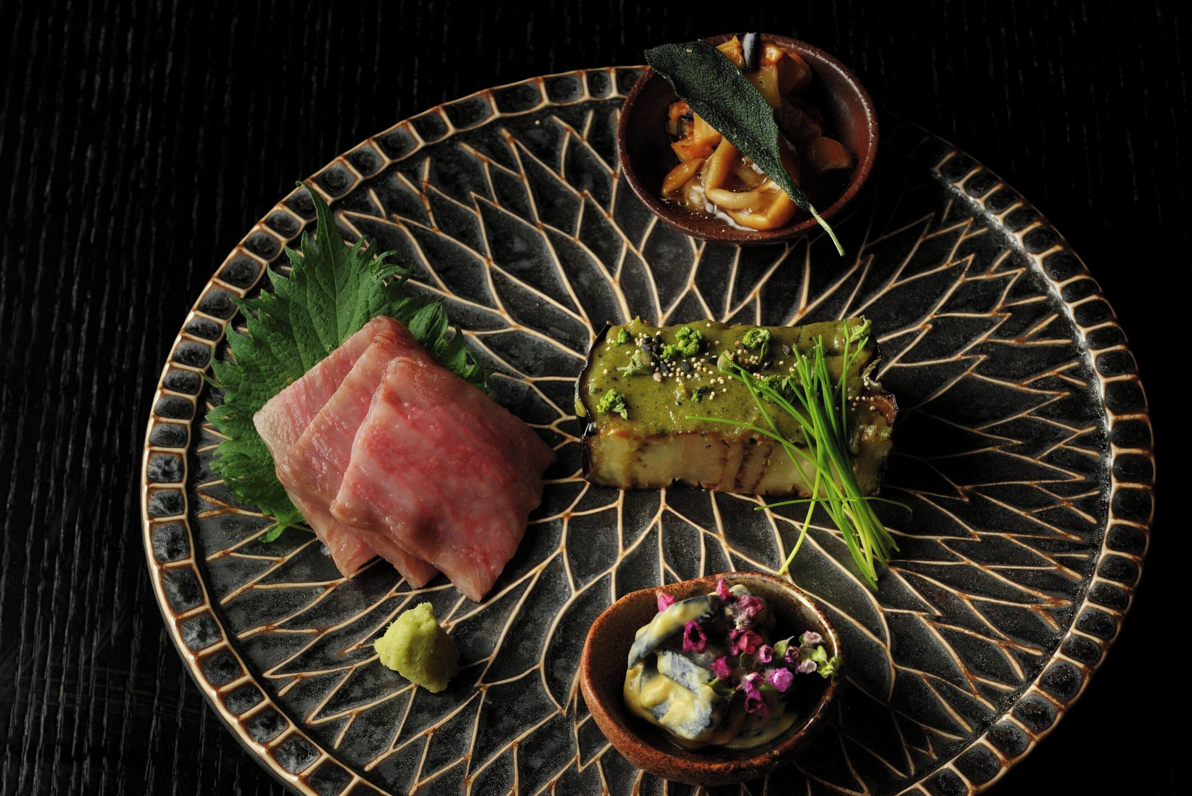 A plate with various food items including sashimi, a piece of grilled fish, and a bowl of pickled vegetables.