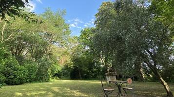 Ein Garten mit Tisch und Stühlen, umgeben von Bäumen und Grün.