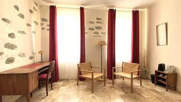 A room with a wooden desk, two chairs, a floor lamp, and a small table with a vase and a coffee maker.