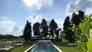 A rectangular swimming pool with a tiled deck, surrounded by grass and trees.