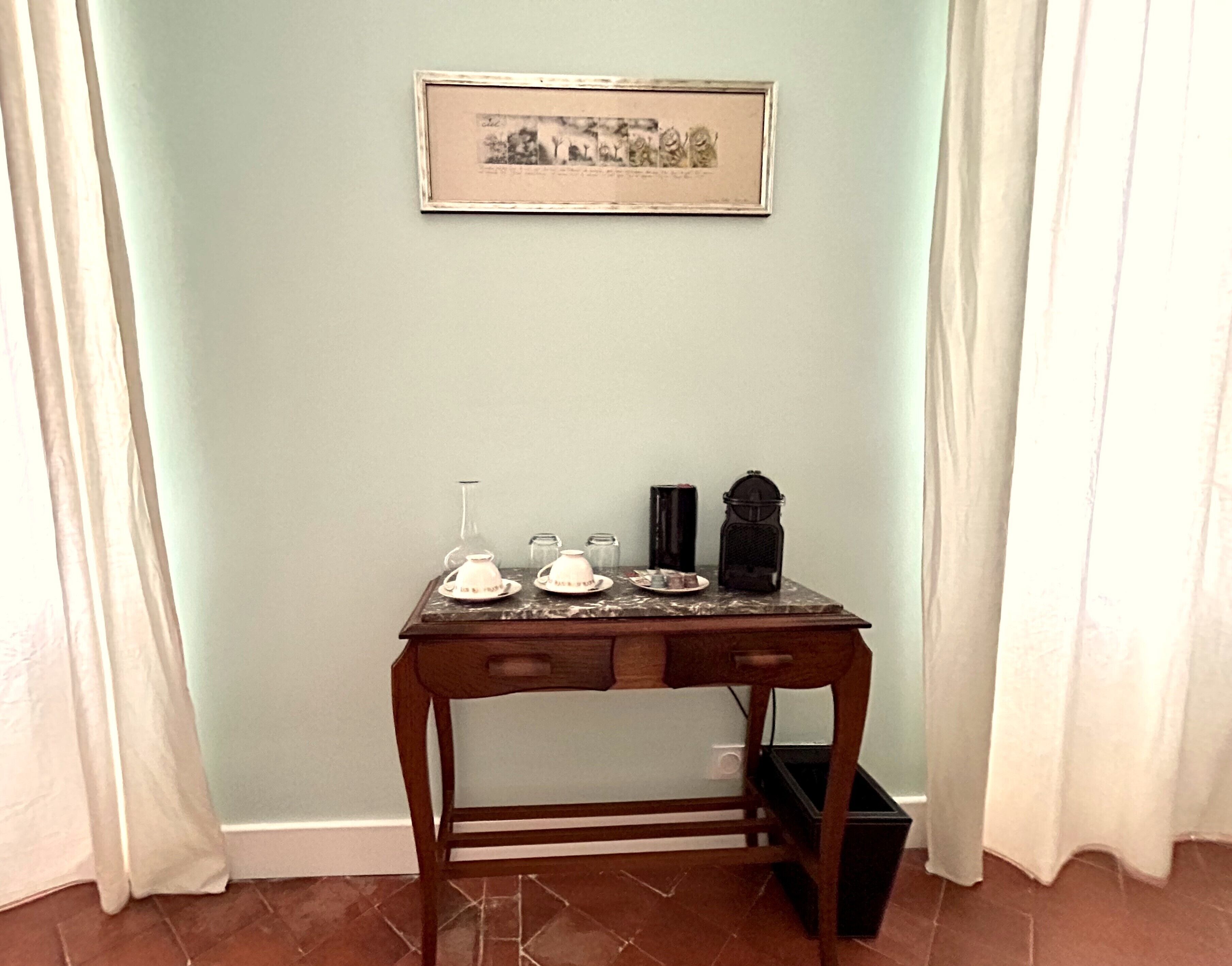 Une petite table en bois, avec un tableau encadré accroché au-dessus, un vase et une bougie posés sur la table.