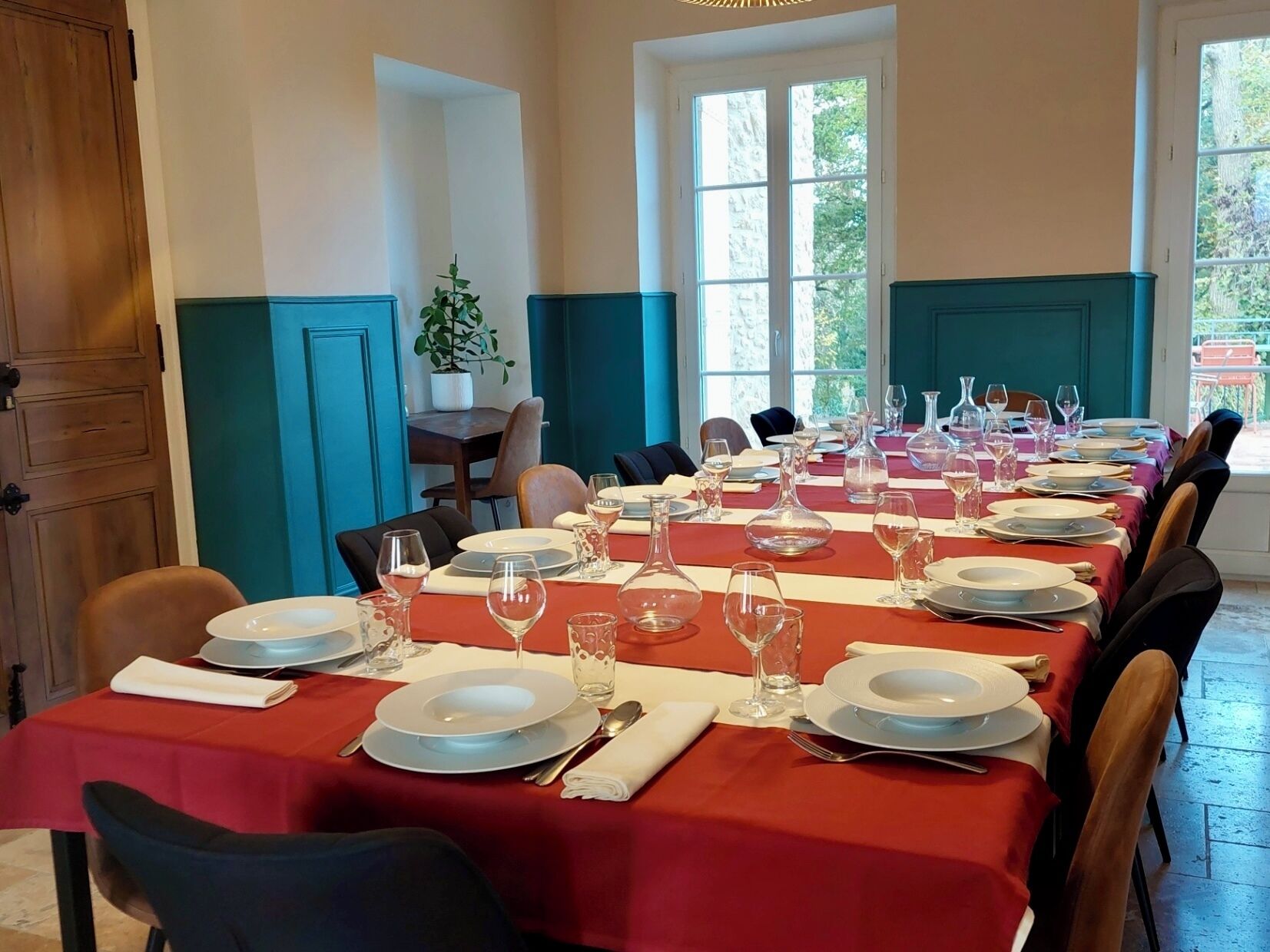 Ein Esszimmer mit gedeckten Tischen, mit rotem Tischlaken, weißen Tellern und klaren Gläsern.