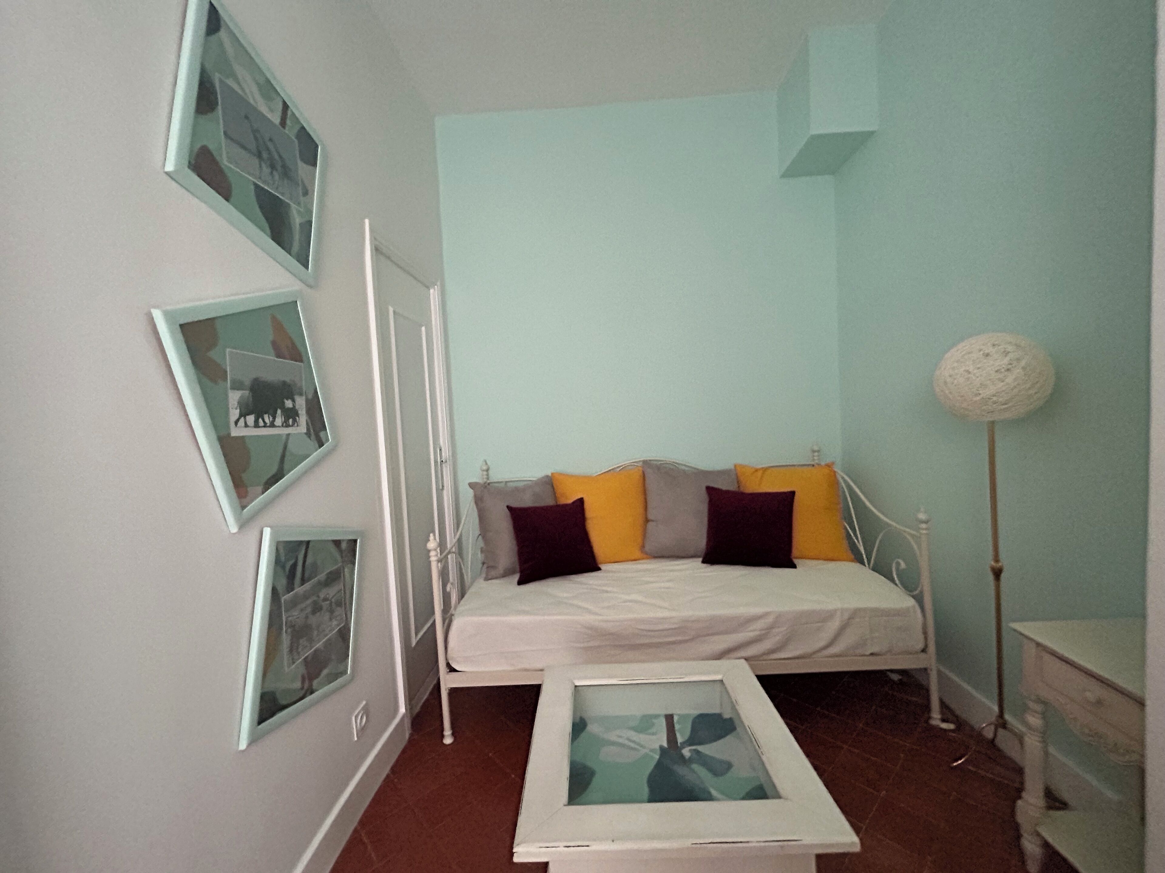 Een slaapkamer met een bed, kussens, een nachtkastje en lijstjes met afbeeldingen aan de muur.