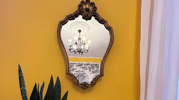 Una habitación con una pared amarilla, una mesa blanca, una planta en maceta, un espejo en marco y una pequeña figurita.