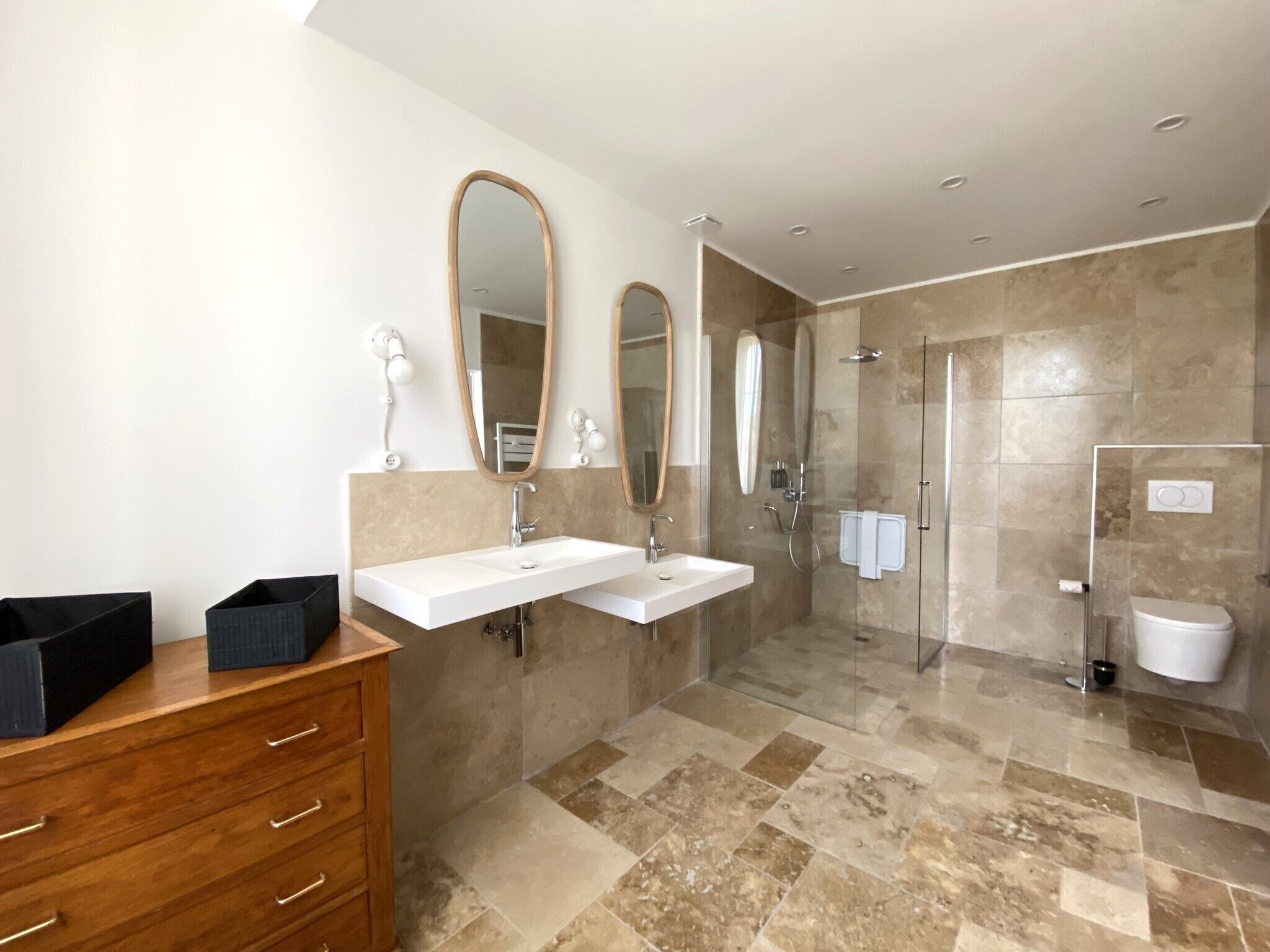 A modern bathroom with a large vanity, two mirrors, a shower, and a toilet.