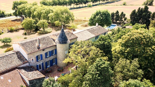 A large stone building with a tower, surrounded by trees and fields.