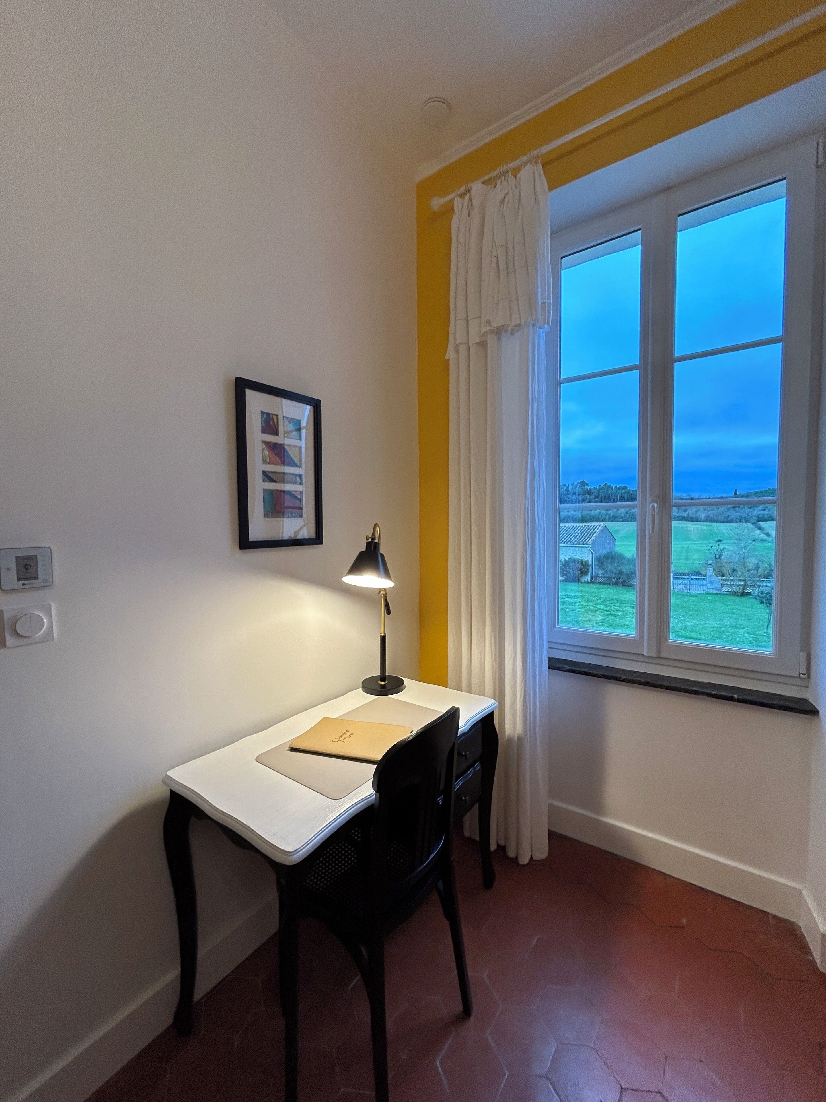 Ett litet rum med ett skrivbord, en stol och ett fönster med gardiner.