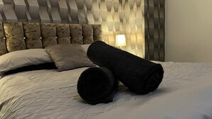 Un lit bien fait, avec des serviettes pliées, une tête de lit capitonnée et une lampe de chevet.