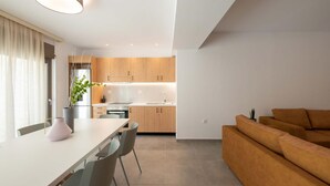Une cuisine moderne avec des meubles en bois, un coin repas avec une table et des chaises, et un canapé marron dans l’espace salon.