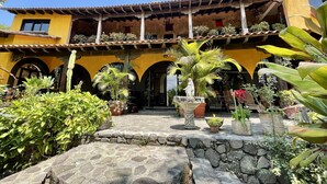 A courtyard with a yellow building, stone steps, and various potted plants.