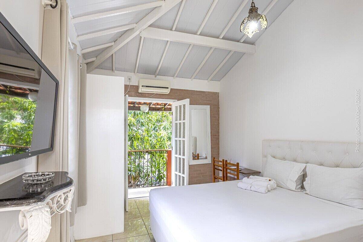 Une chambre d’hôtel équipée d’un lit, d’une télévision, d’un balcon avec vue sur la verdure et d’un ventilateur de plafond.