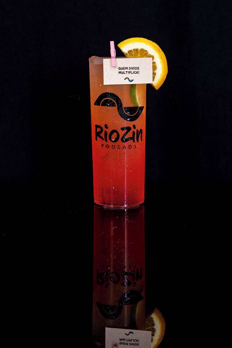 Un vaso alto con una bebida roja y una rodaja de limón como adorno, etiquetado 'Riozin,' sobre un fondo oscuro.