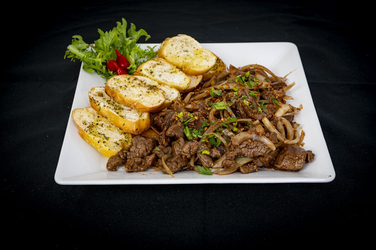 Un plato de salteado de carne con cebollas y hierbas, acompañado de pan con ajo y una ensalada.