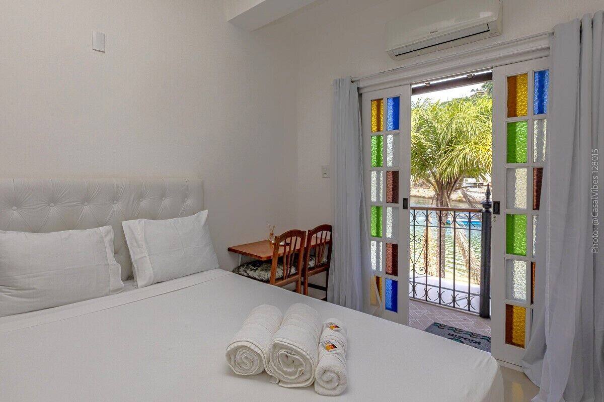 Une chambre d’hôtel avec un lit, une petite table et une chaise. Il y a une fenêtre avec des vitraux colorés et une vue sur les palmiers à l’extérieur.