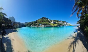 Escena costera con un mar azul transparente, una playa arenosa y un puente.