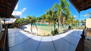 A beach view from a covered area with a pool and palm trees. - RioZin Pousada Liberal - Adults Only - Clothing Optional (Rio de Janeiro)