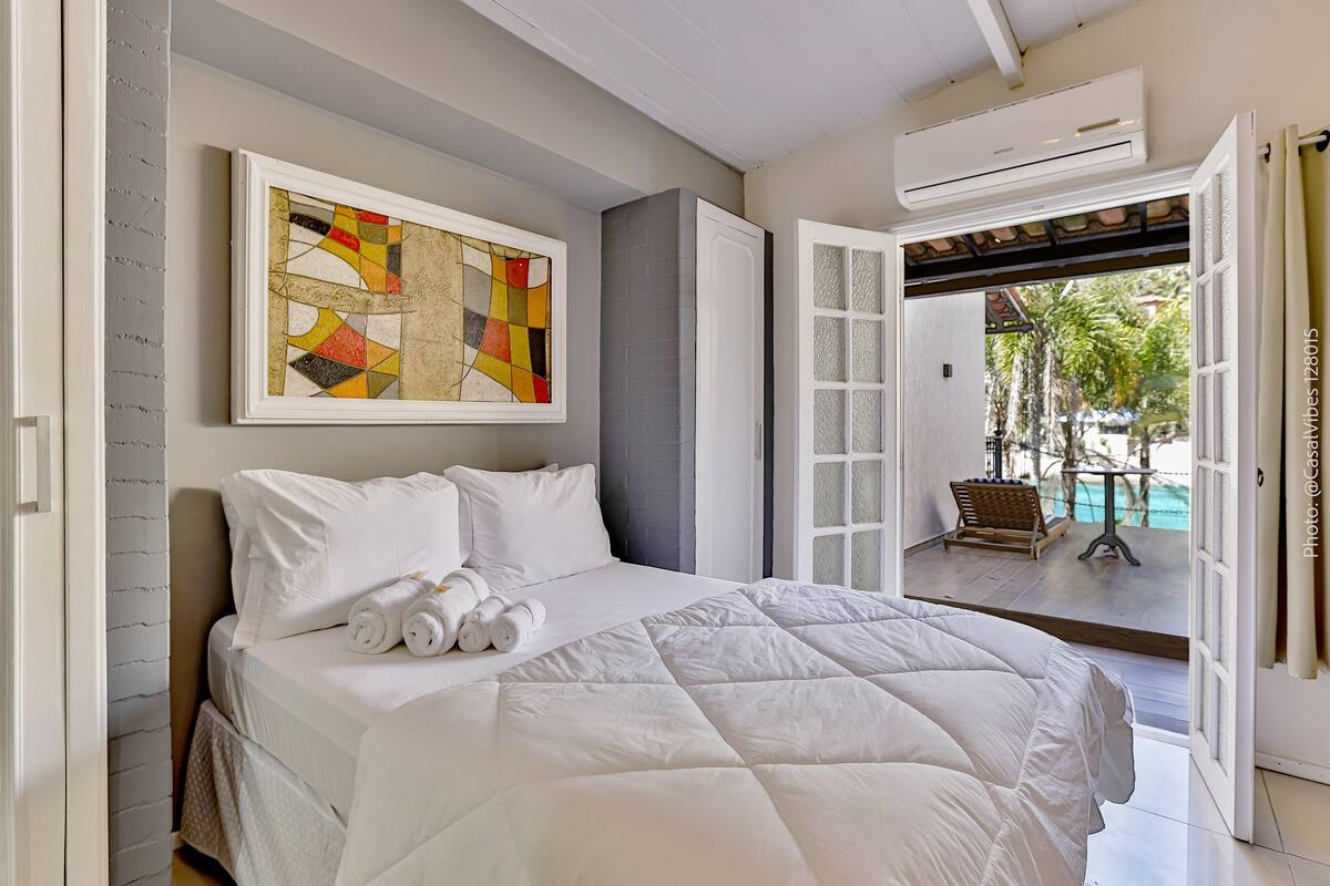 Une chambre d’hôtel avec un grand lit, un tableau accroché au mur et une porte ouverte donnant sur un espace piscine.