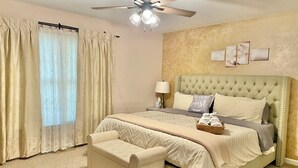 A bedroom with a large bed, a nightstand, a lamp, a ceiling fan, and a window with curtains. - Cozy house in Ocean pines, only 10 mins away from Ocean City. (Ocean Pines)