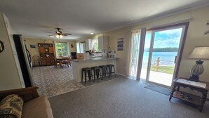 Amplia sala de estar con cocina, comedor y un amplio ventanal corredizo que da a un balcón con vistas al lago.