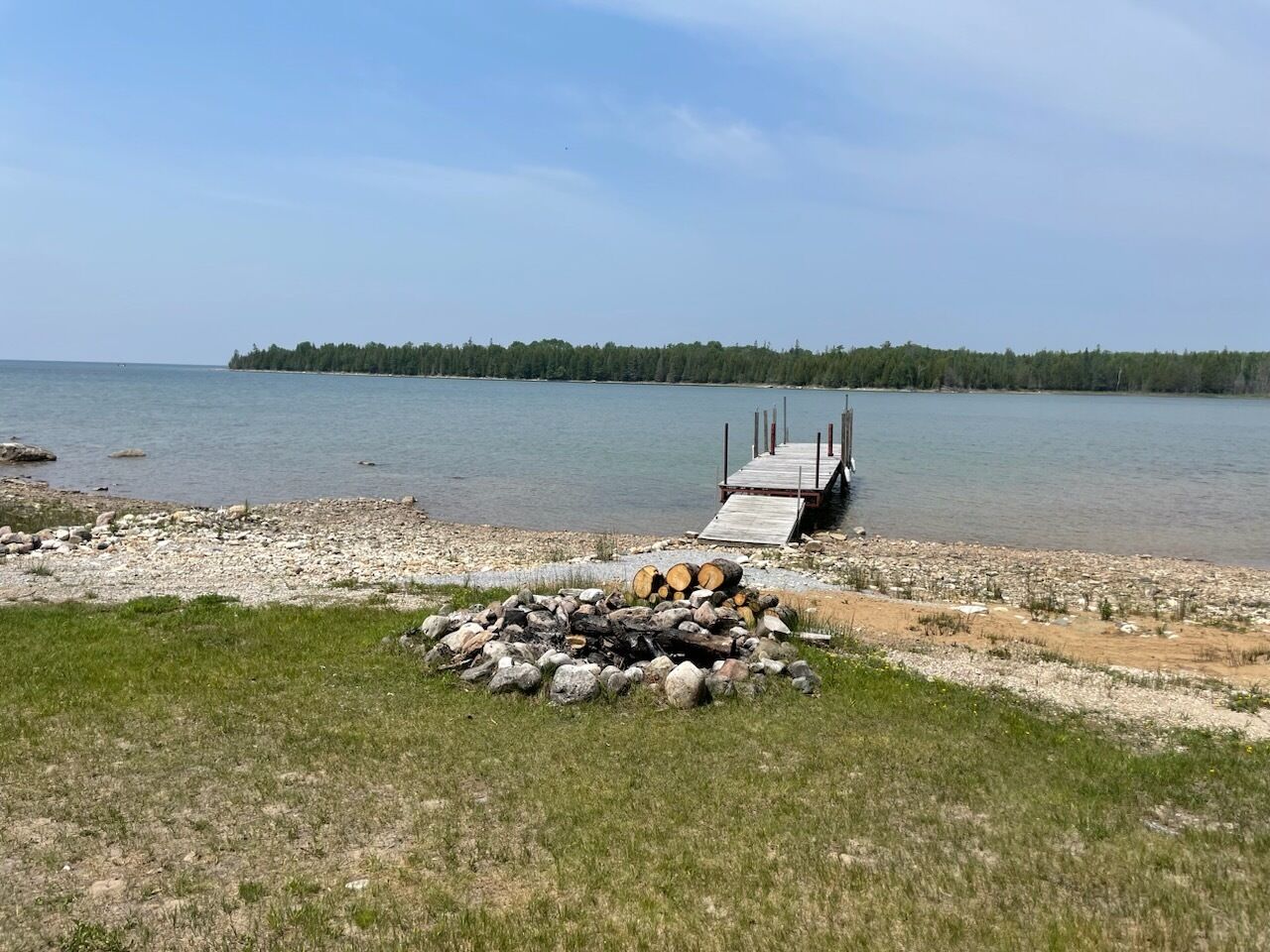 Un muelle a orillas del lago con un hogar para fogatas y un espigón de madera que se adentra en el agua.